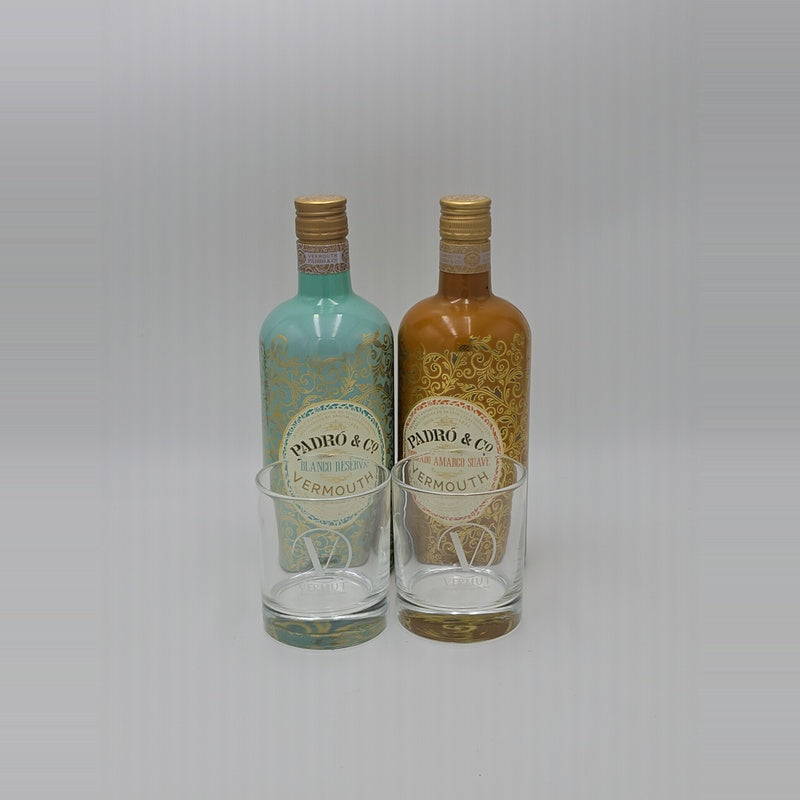 Two Pedro & Co Vermoutain bottles, one with a turquoise-blue glass and one with an amber-brown glass, each paired with a clear glass decanter, set against a neutral light gray background.